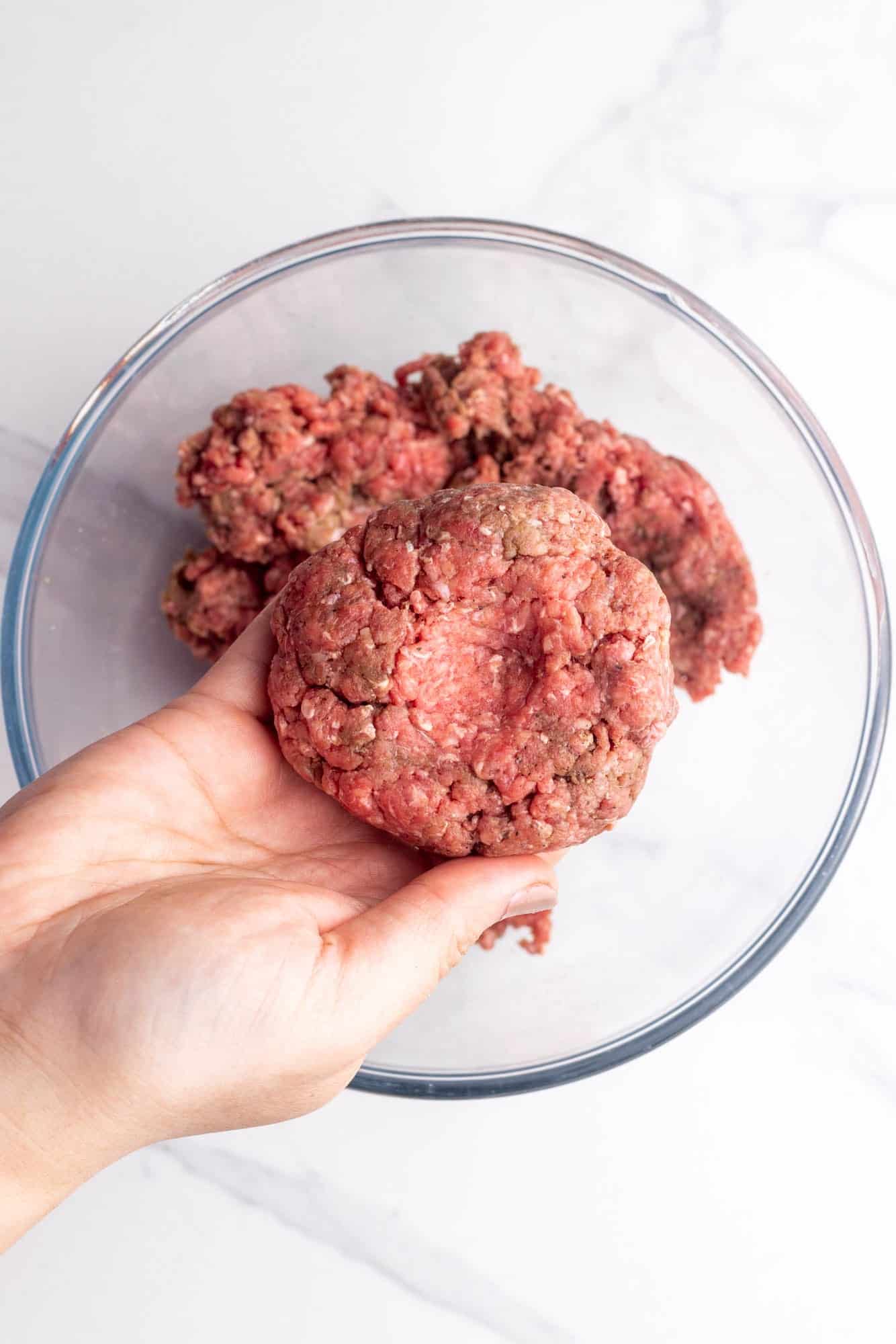 Hand holding a shaped hamburger patty over a bowl of seasoned ground beef