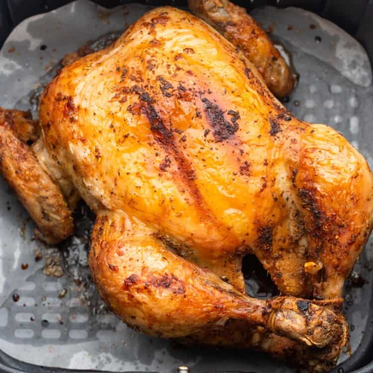 Overhead shot of a whole roast chicken in an air fryer basket lined with parchment paper liner