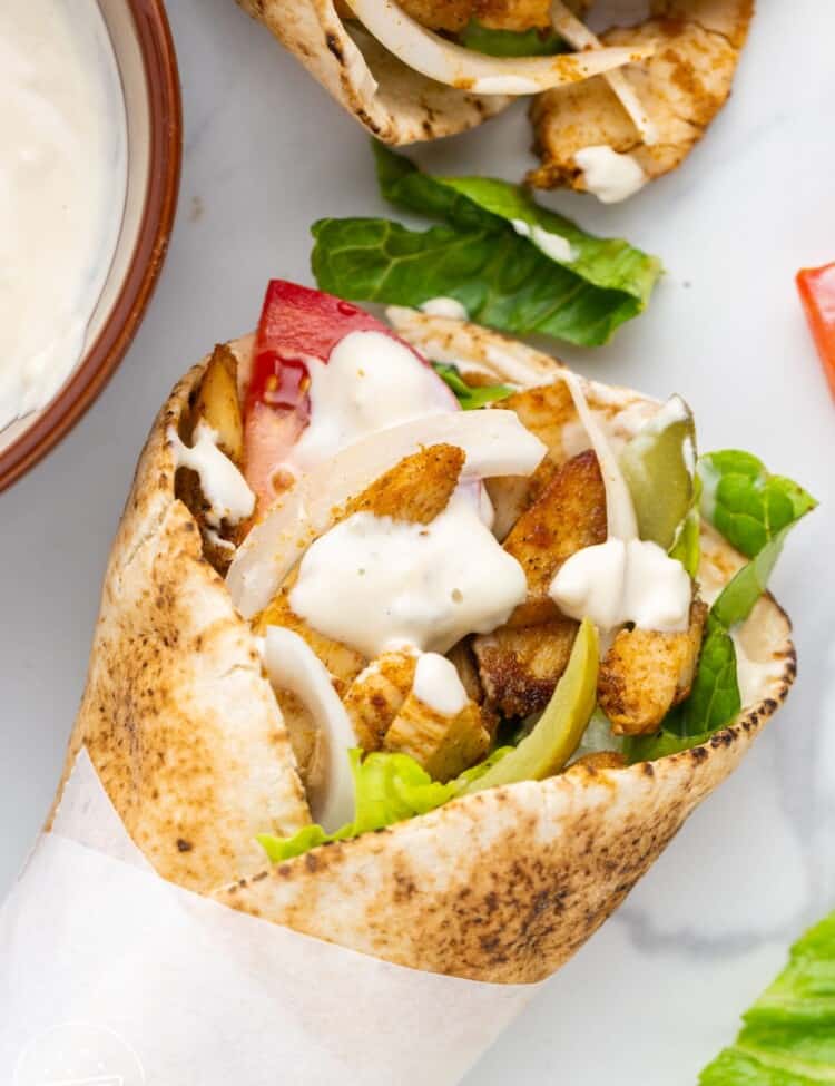 chicken shawarma in a wrap with onions, lettuce, and tomato.