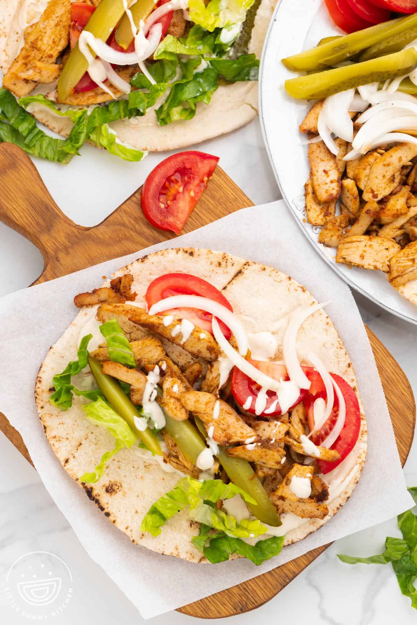 a pita on a cutting board, with chicken shawarma fillings on it.