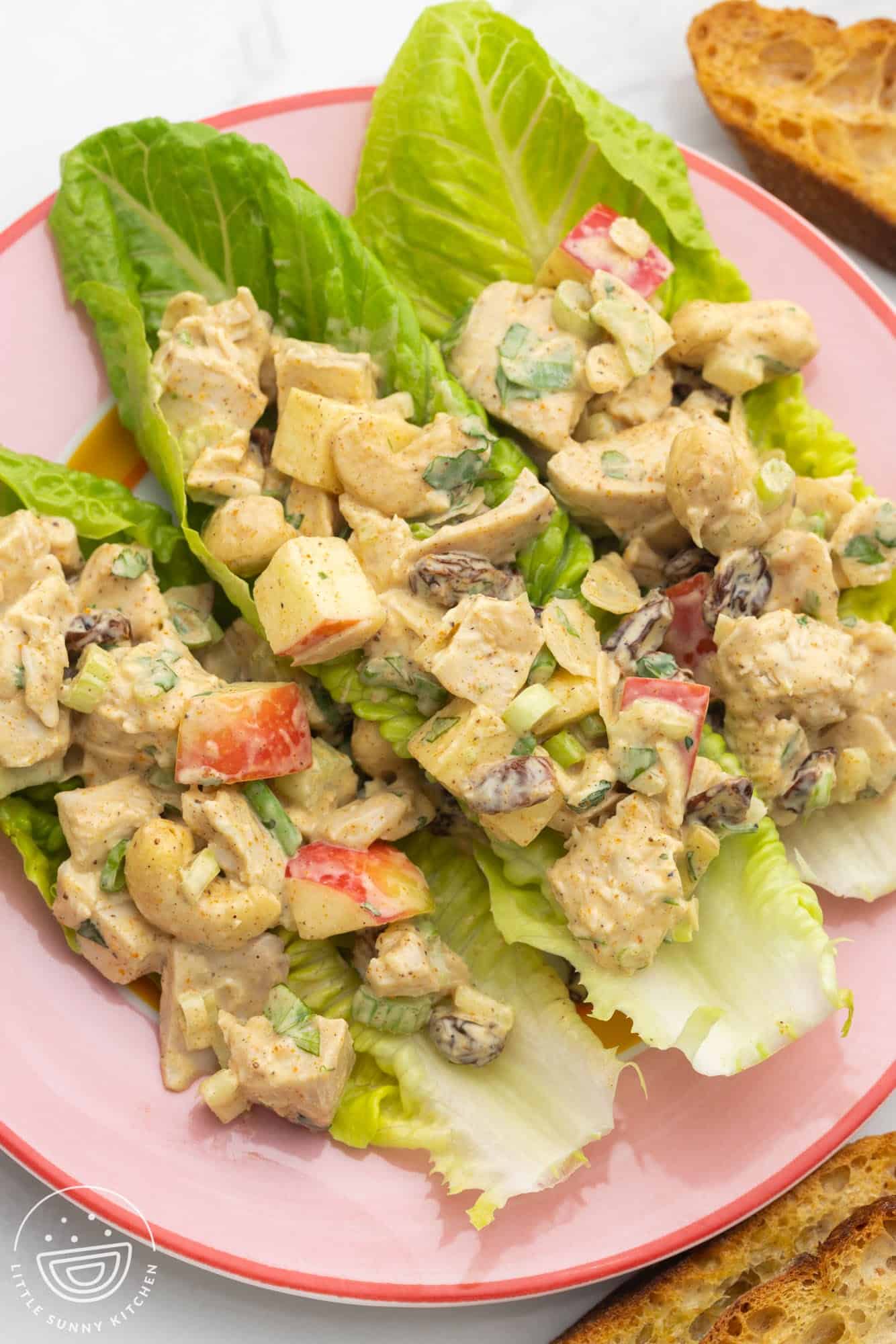 three romaine leaves on a plate, filled with curry chicken salad