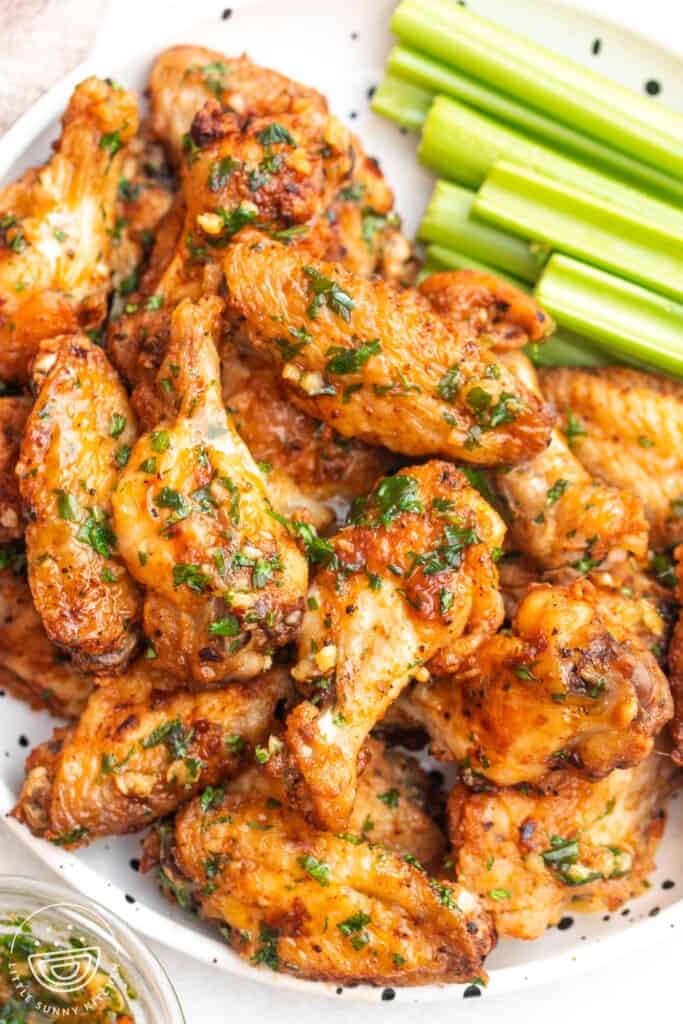 Overhead shot garlic butter chicken wings on a white speckled plate, with celery sticks on the side.