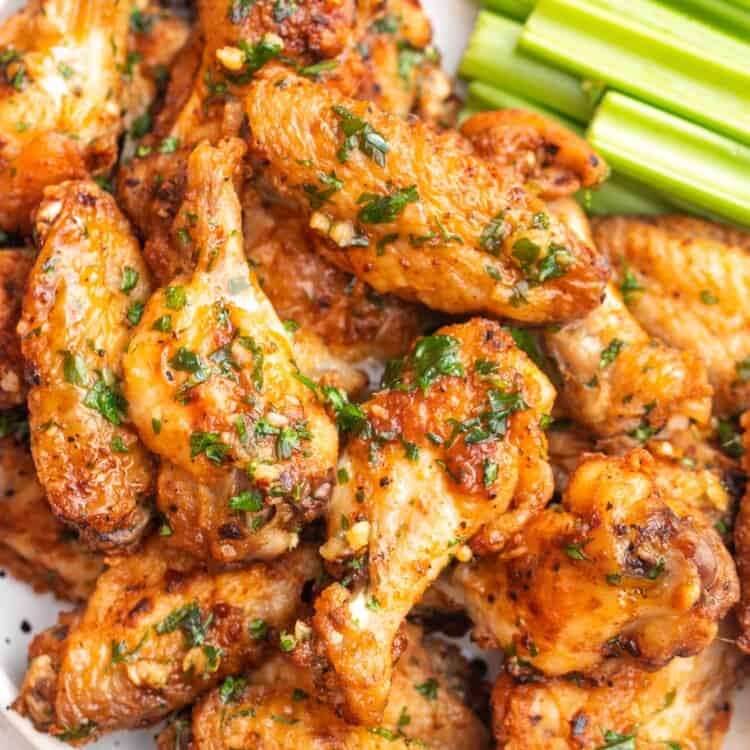 Overhead shot garlic butter chicken wings on a white speckled plate, with celery sticks on the side.