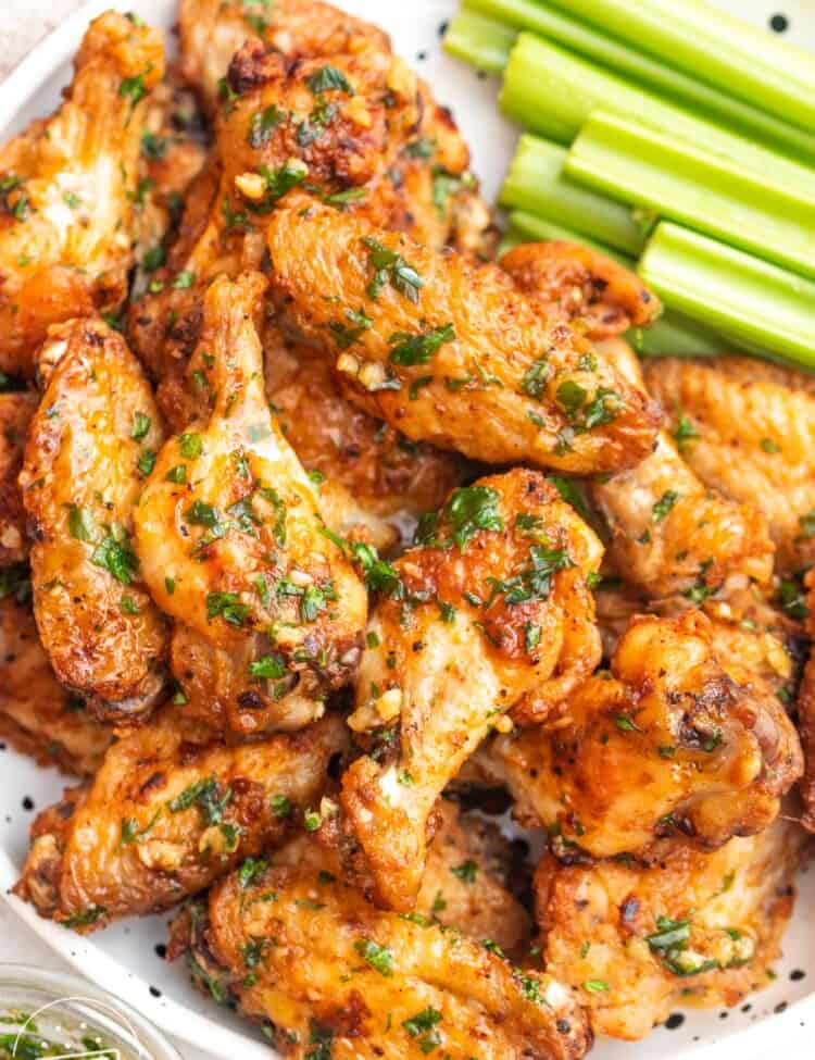 Overhead shot garlic butter chicken wings on a white speckled plate, with celery sticks on the side.