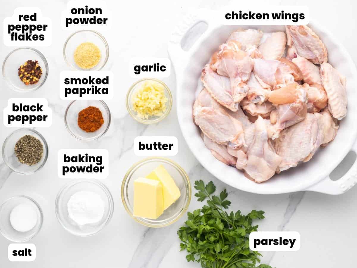 Ingredients needed to make garlic butter chicken wings including chicken wings, parsley, butter, garlic, onion powder, smoked paprika, baking powder, salt, and pepper.