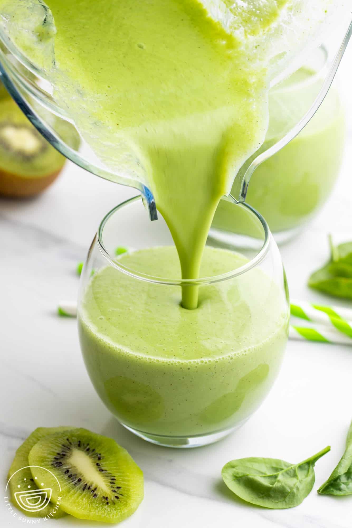 Pouring a green kiwi smoothie into a transparent glass