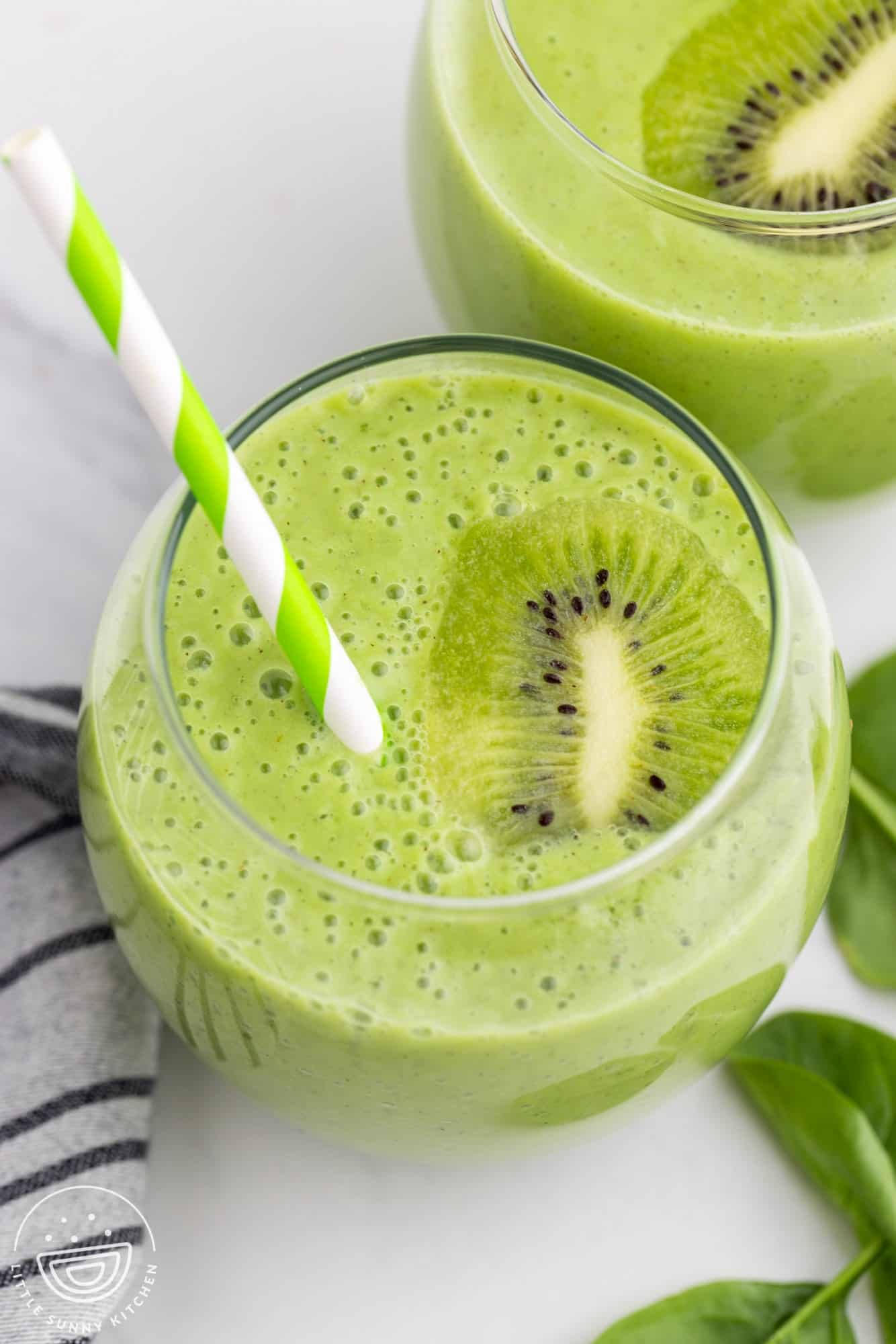 Close up shot of glasses filled with kiwi smoothie, and green straw.