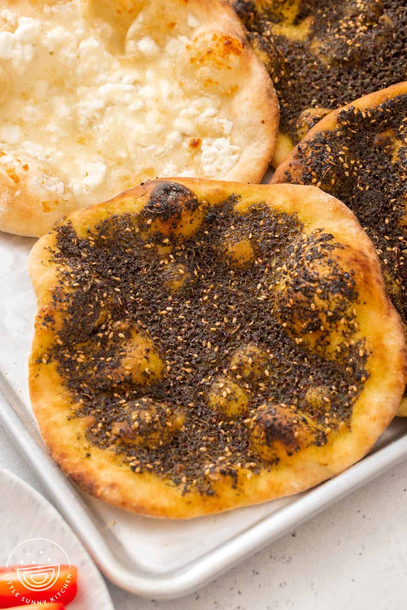 Za'atar manousheh, with a cheese one in the back. Served on a sheet pan.
