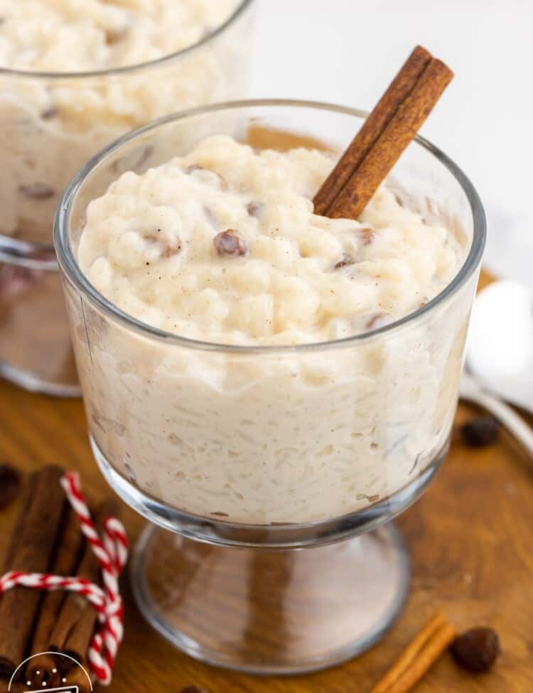 a footed glass dessert dish of rice pudding with a cinnamon stick stuck in it.