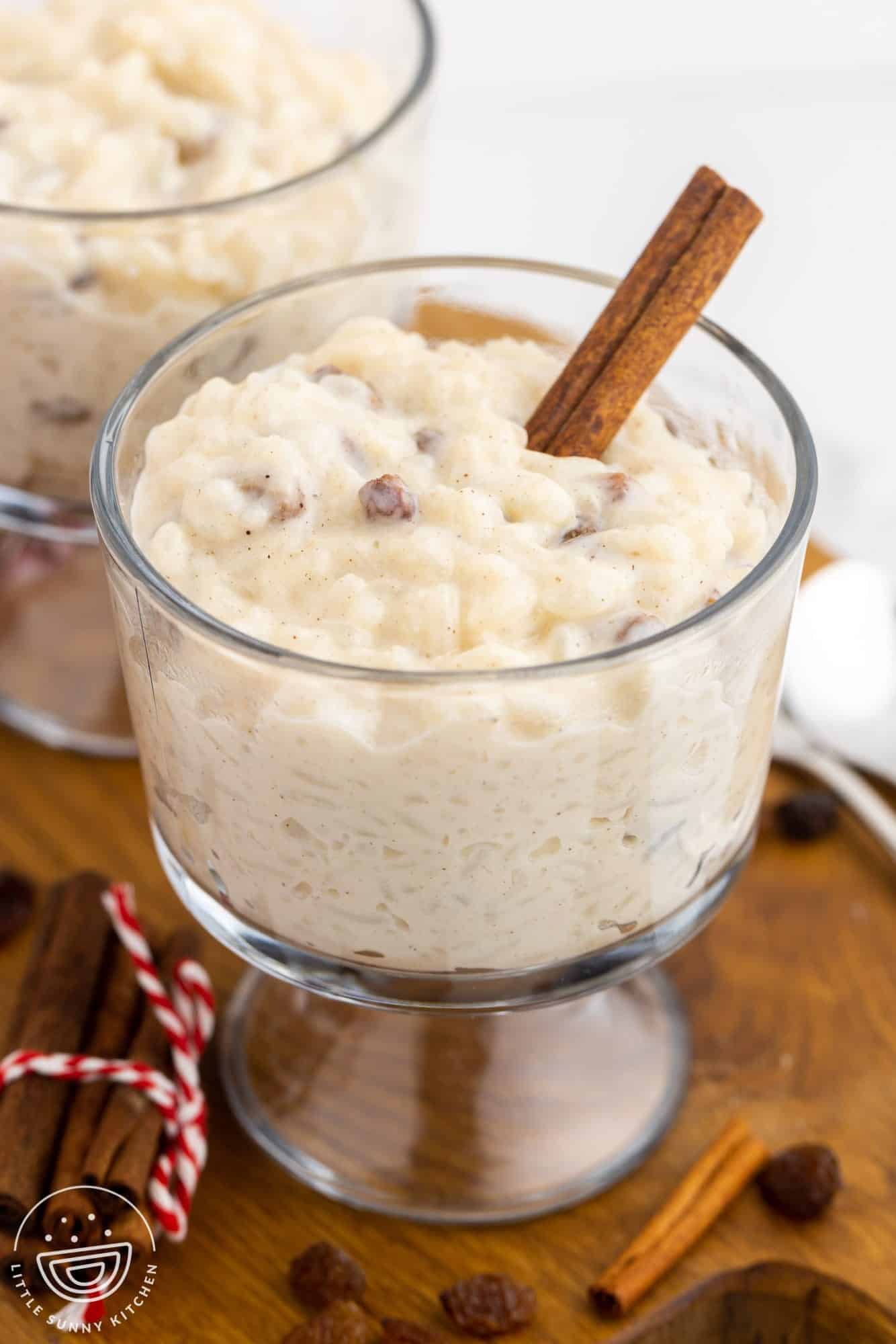 a footed glass dessert dish of rice pudding with a cinnamon stick stuck in it.