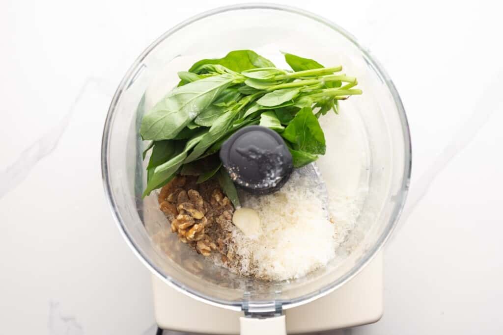 Pesto ingredients in the bowl of a food processor before blending