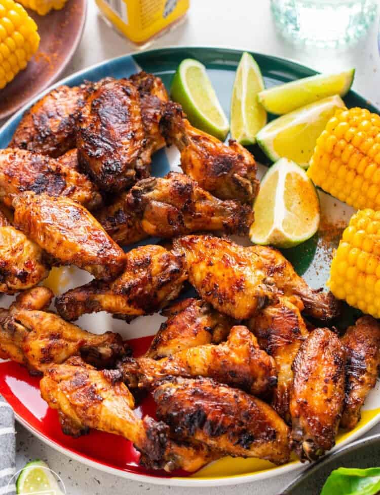 a large plate of peri peri wings with lime wedges and corn on the side.