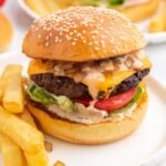 a cheeseburger with lettuce and tomato on a bun, with a side of french fries