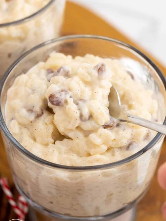 a bowl of homemade rice pudding with raisins. A spoon is lifting up a bite.