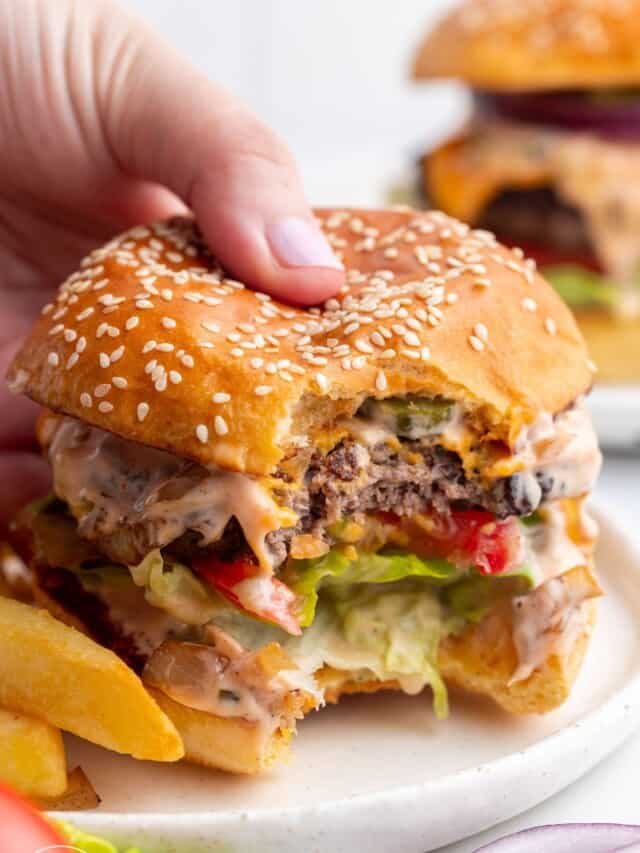 a hand holding a cheeseburger with a bite taken out of it.