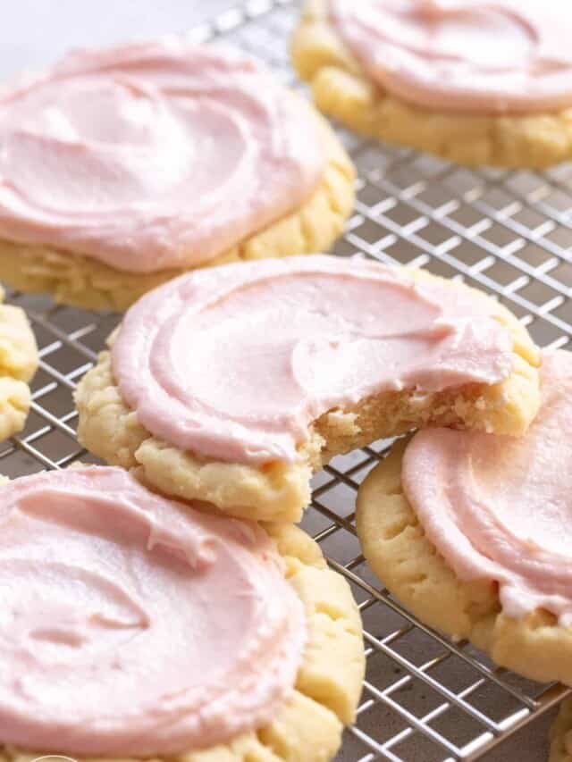 copycat swig sugar cookies with pink frosting, on a wire rack. One cookie has a bite taken