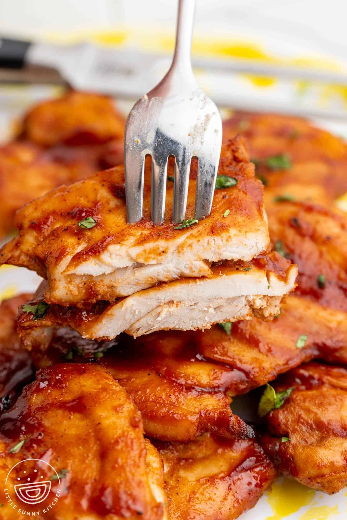 a fork holding sliced bbq chicken thighs to show the interior texture of the meat.