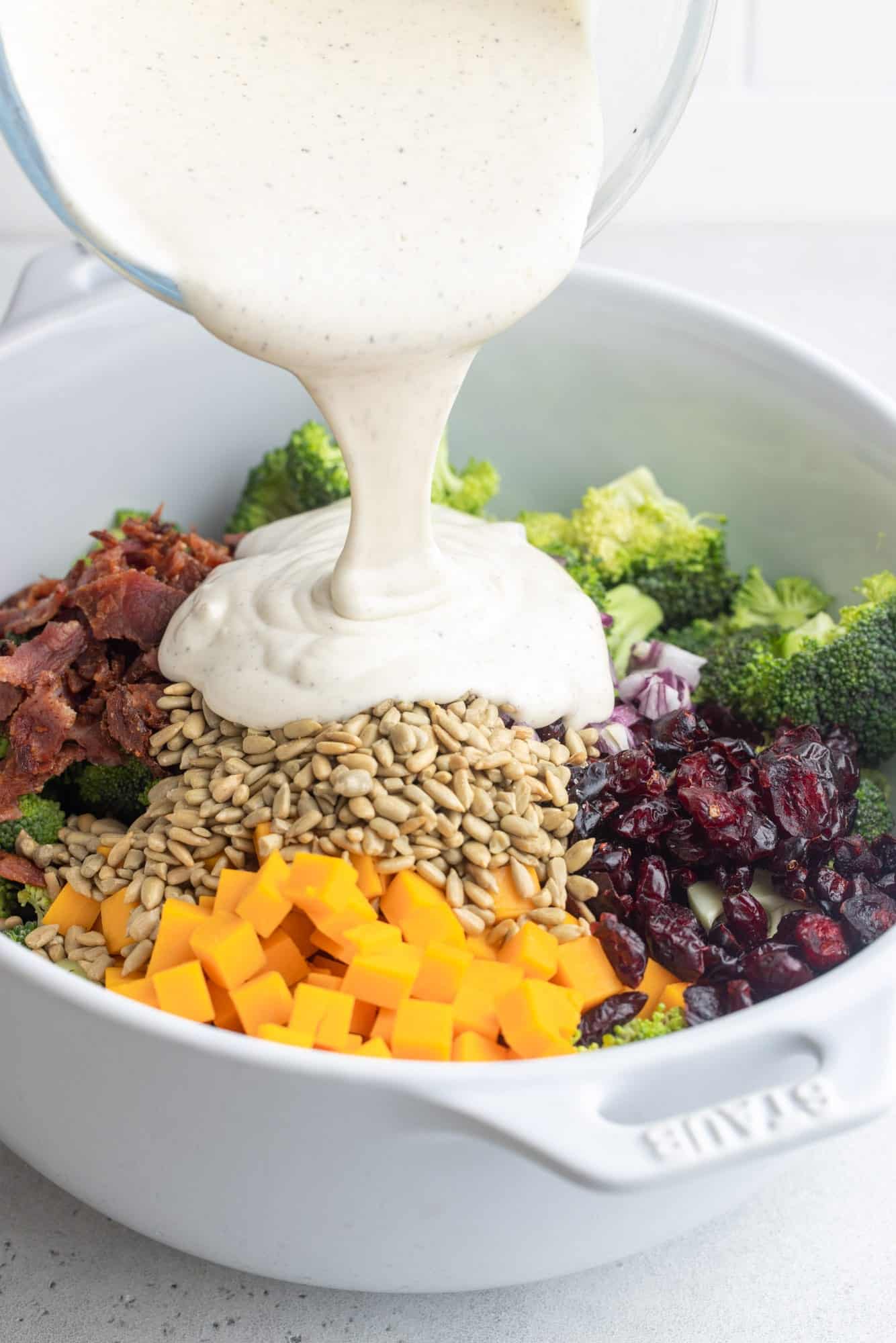 Creamy dressing poured over broccoli, sunflower seeds, cheese, bacon, and cranberries