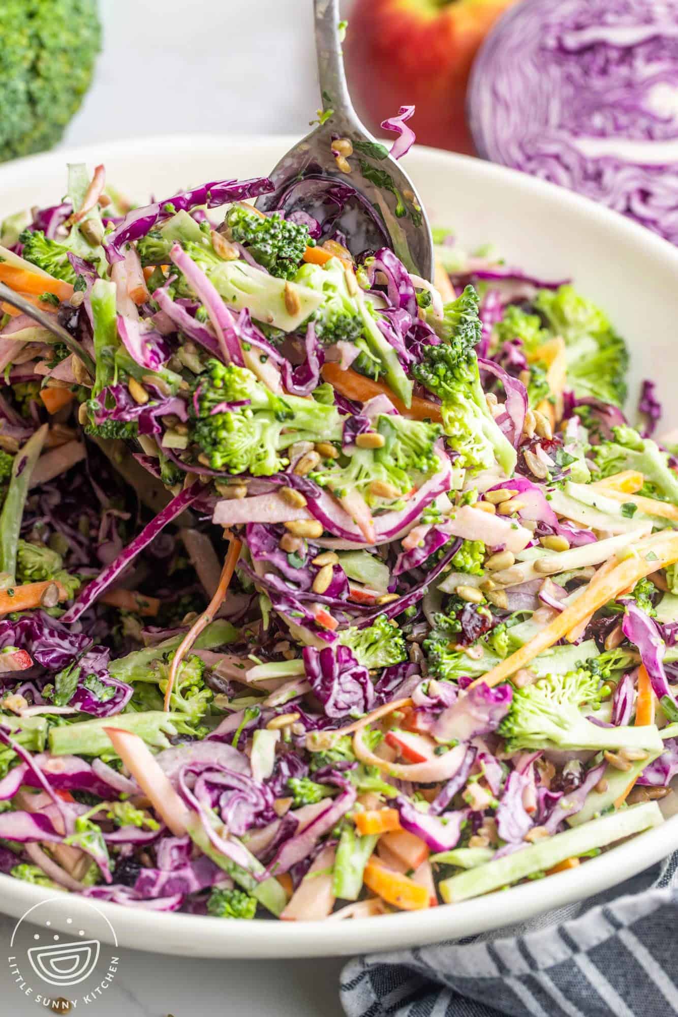 A serving bowl filled with homemade broccoli slaw. A spoon is serving it.