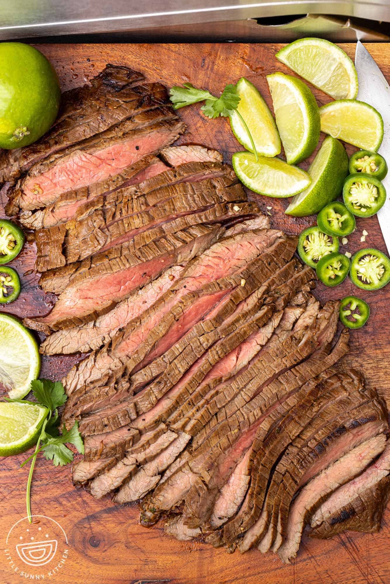 A dark wooden cutting board holding sliced carne asada.