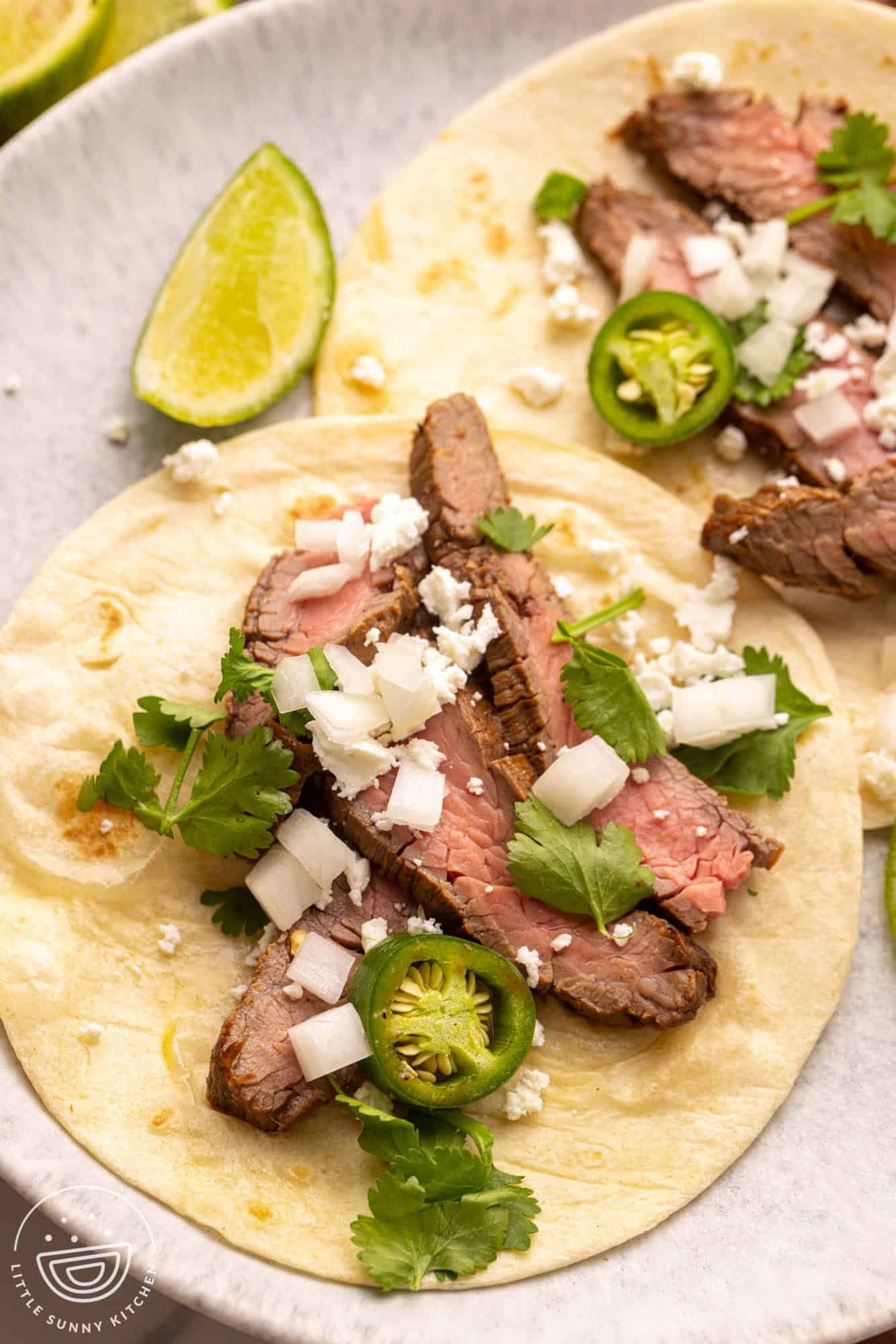 Flour tortillas with sliced carne asada, cotija cheese, onions, cilantro, and jalapenos