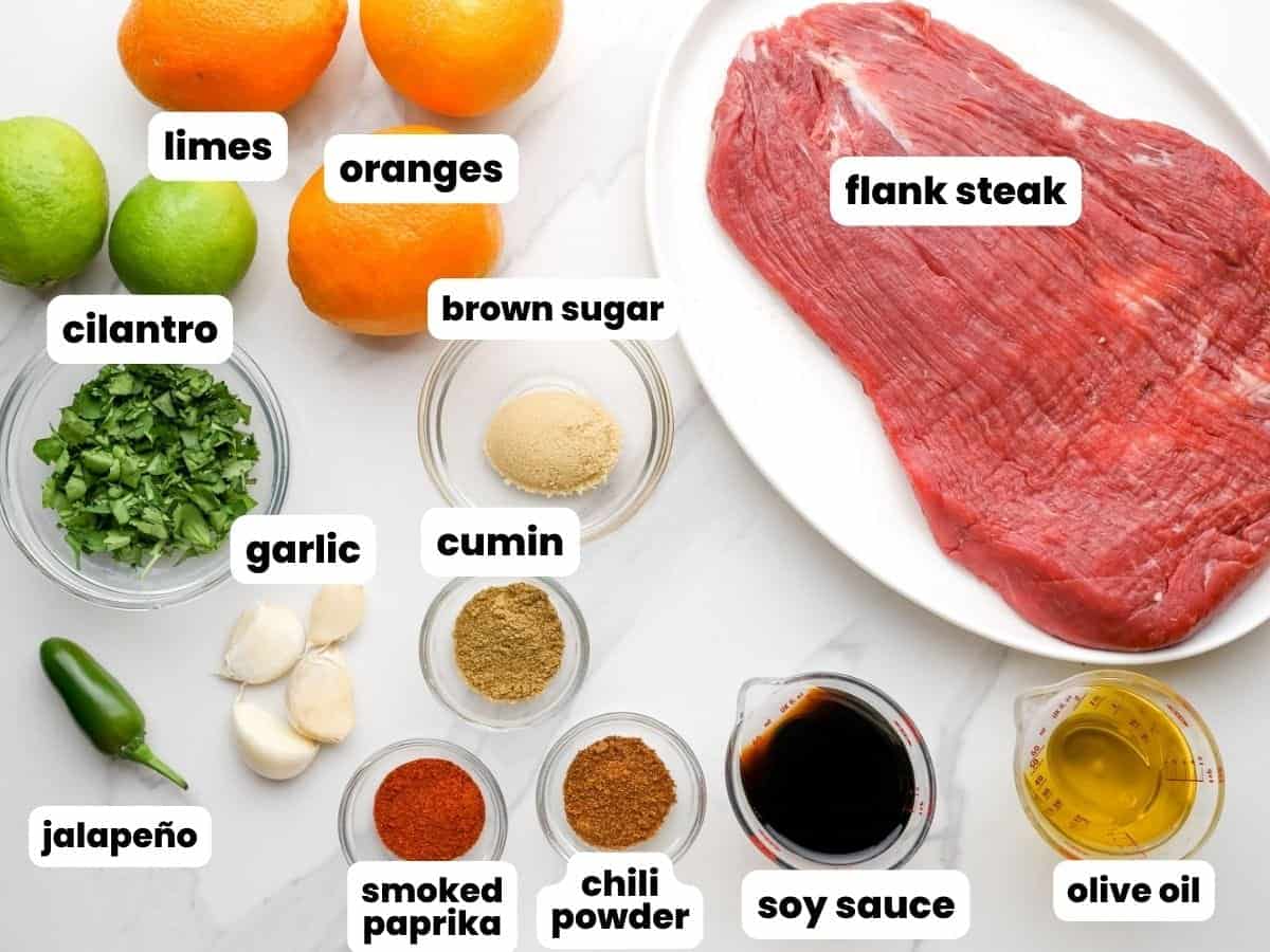 The ingredients for carne asada, including a flank steak, limes and oranges, brown sugar, cilantro, and spices.