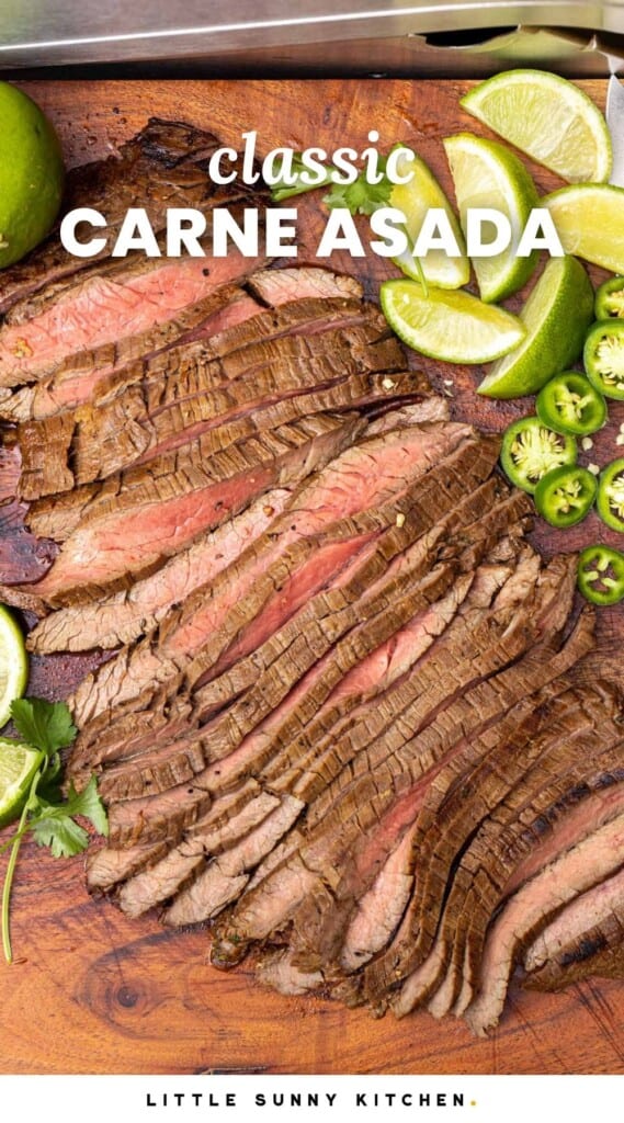A wooden cutting board of sliced carne asada with lime wedges and sliced jalapeno