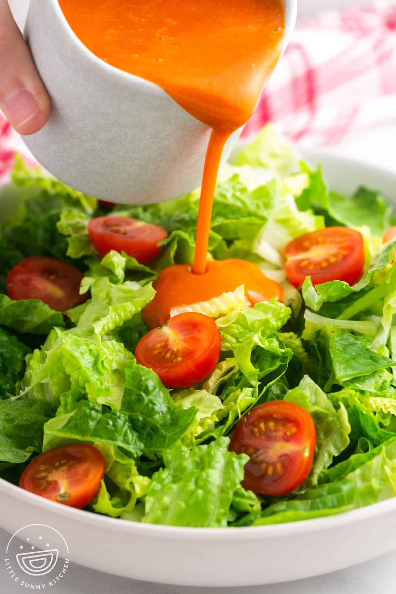 Pouring Catalina dressing over a simple salad of leafy greens and cherry tomatoes