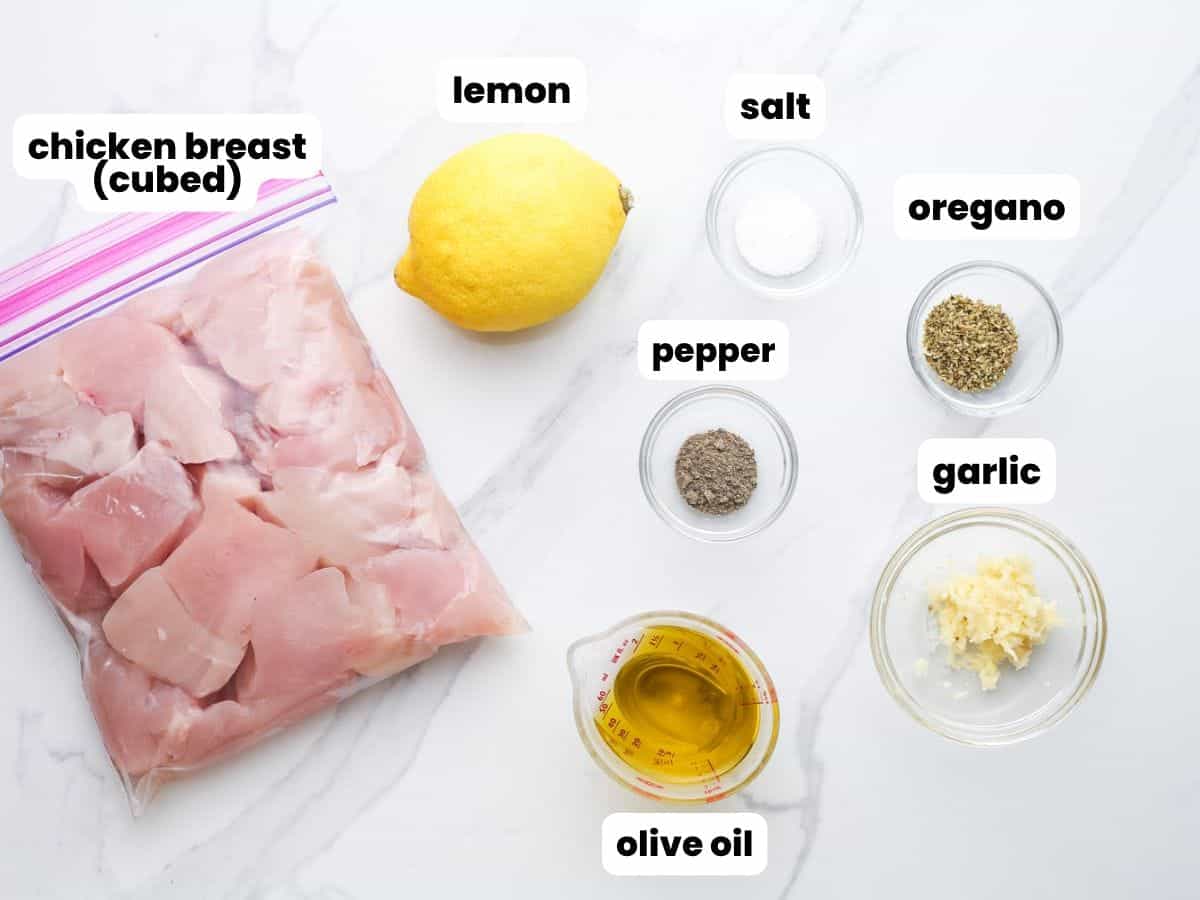 The ingredients needed to make chicken souvlaki, including cubed chicken breast in a ziplock bag, lemon, garlic, and oregano.