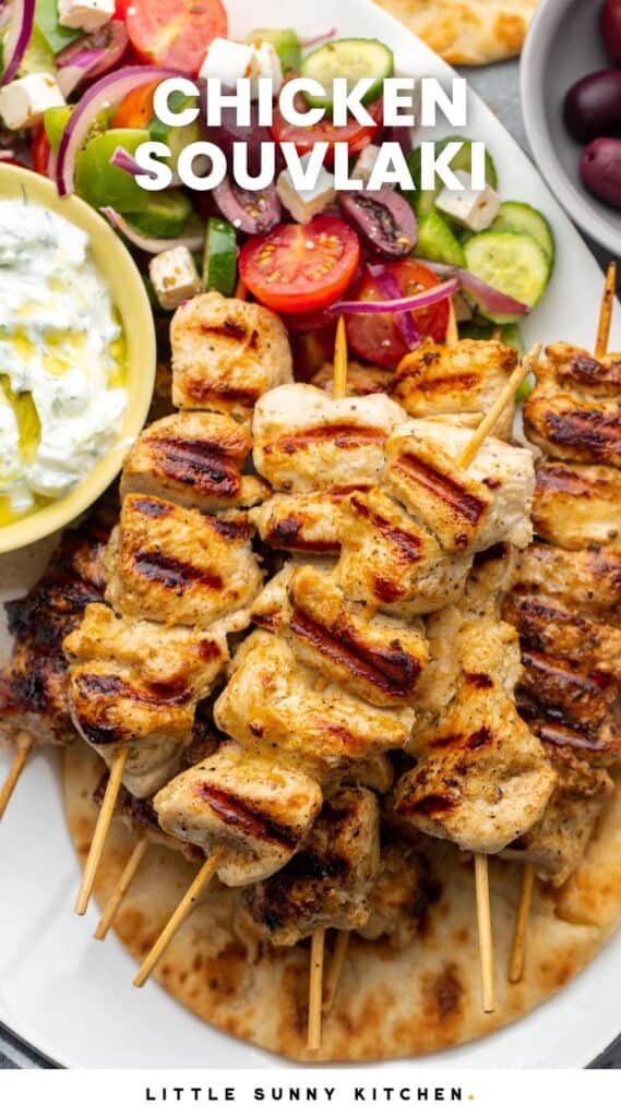 chicken skewers on a platter with salad and sauce. Text overlay says "chicken souvlaki"