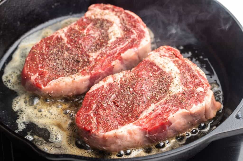 Ribeye steaks searing in a pan.