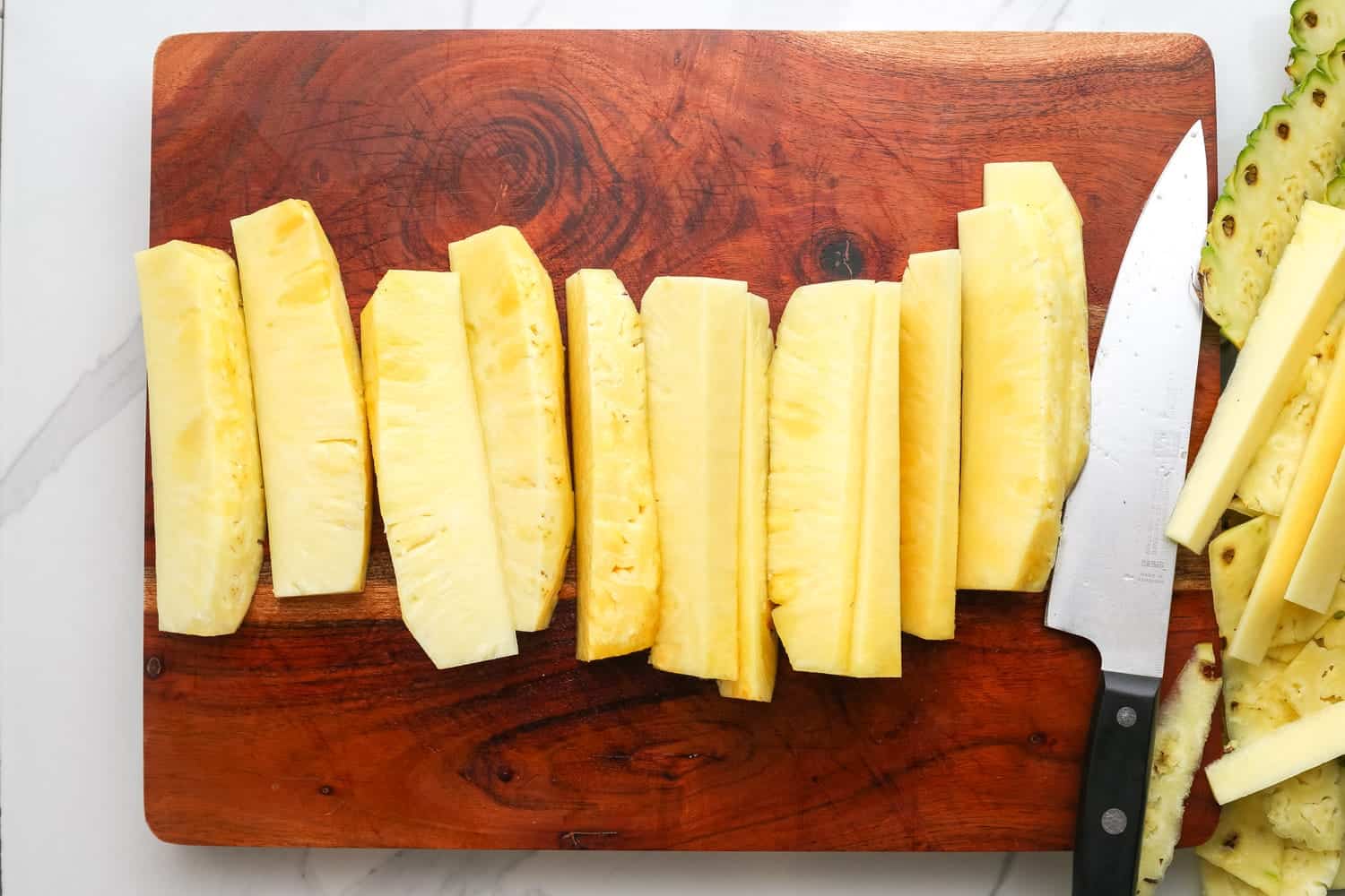 Sliced pineapple into spears on a cutting board, with a chef's knife on the side.