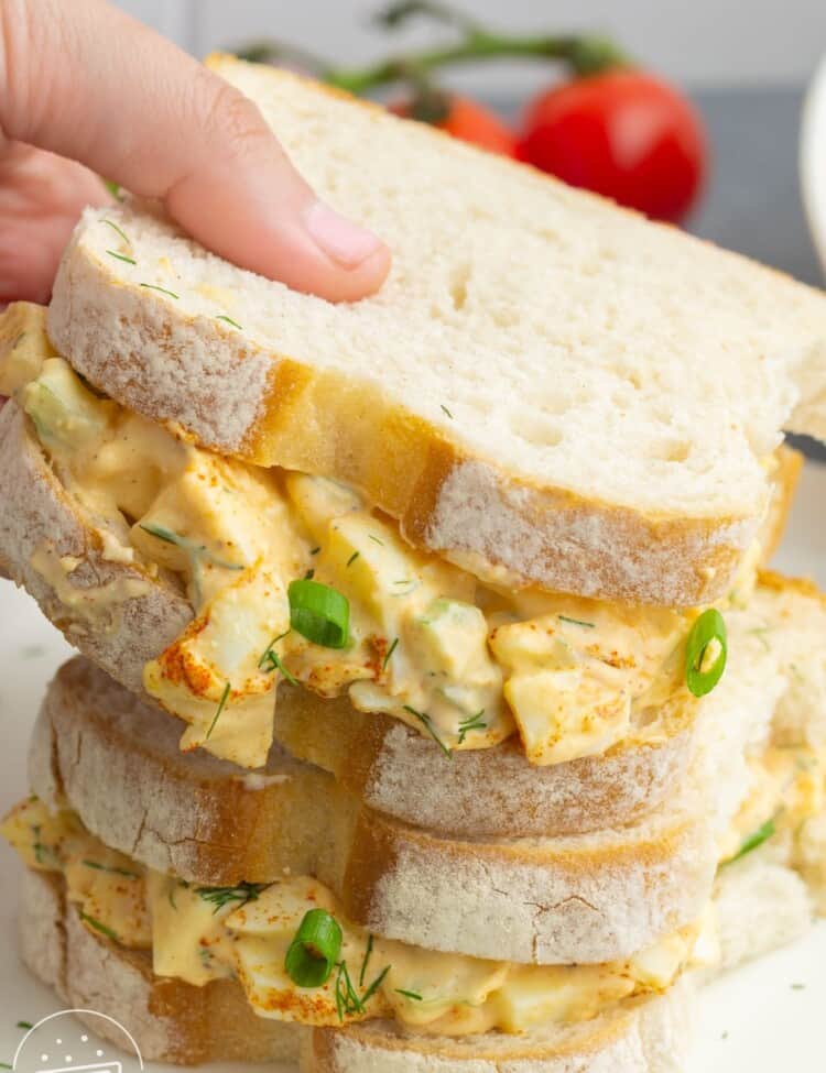 Two egg salad sandwiches on country white bread, stacked on top of one another.
