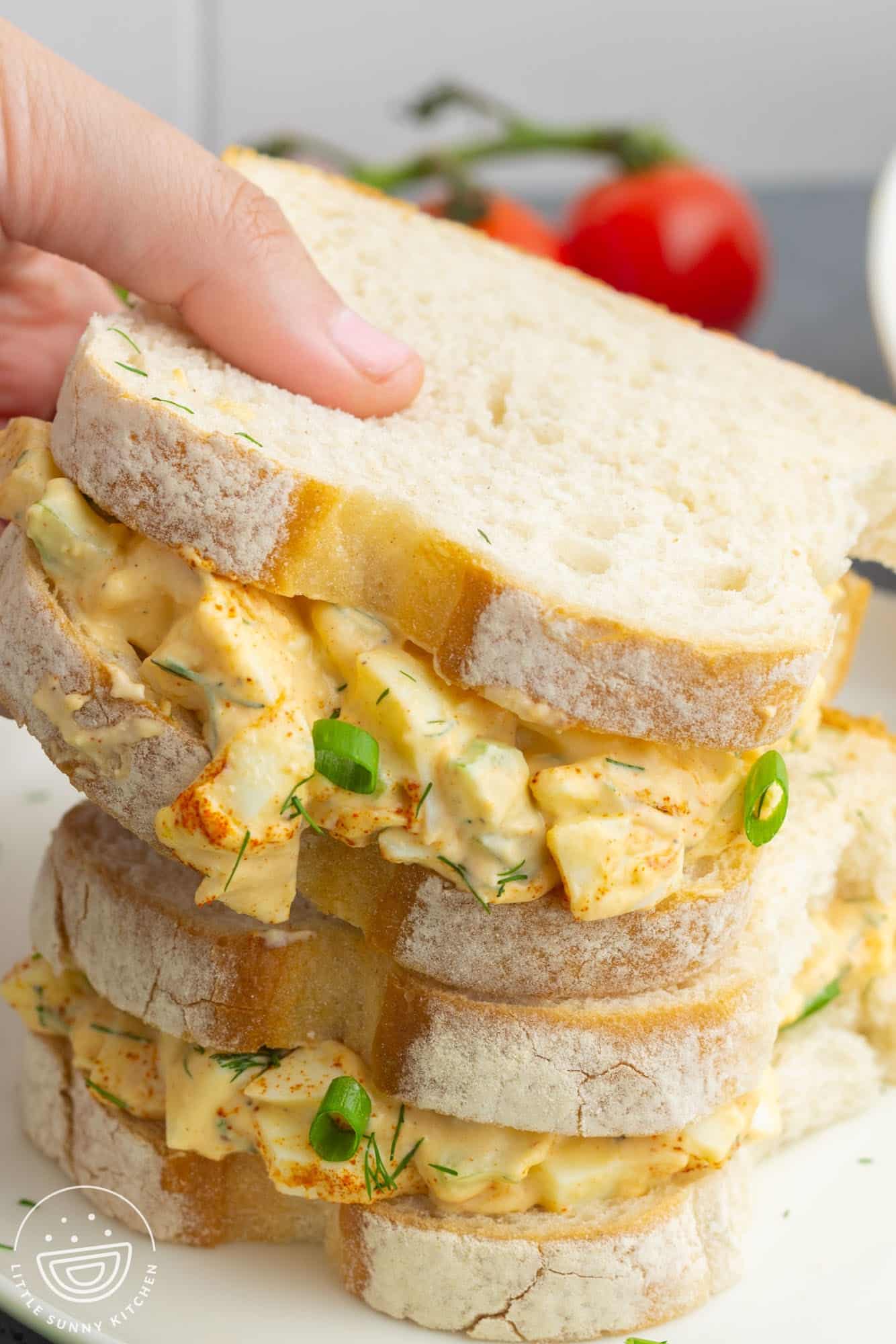 Two egg salad sandwiches on country white bread, stacked on top of one another.