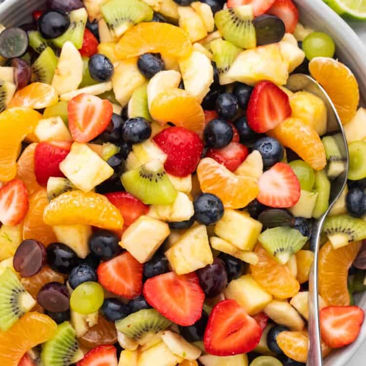 Overhead shot of a fruit salad with lime honey dressing in a large gray bowl, and a serving spoon