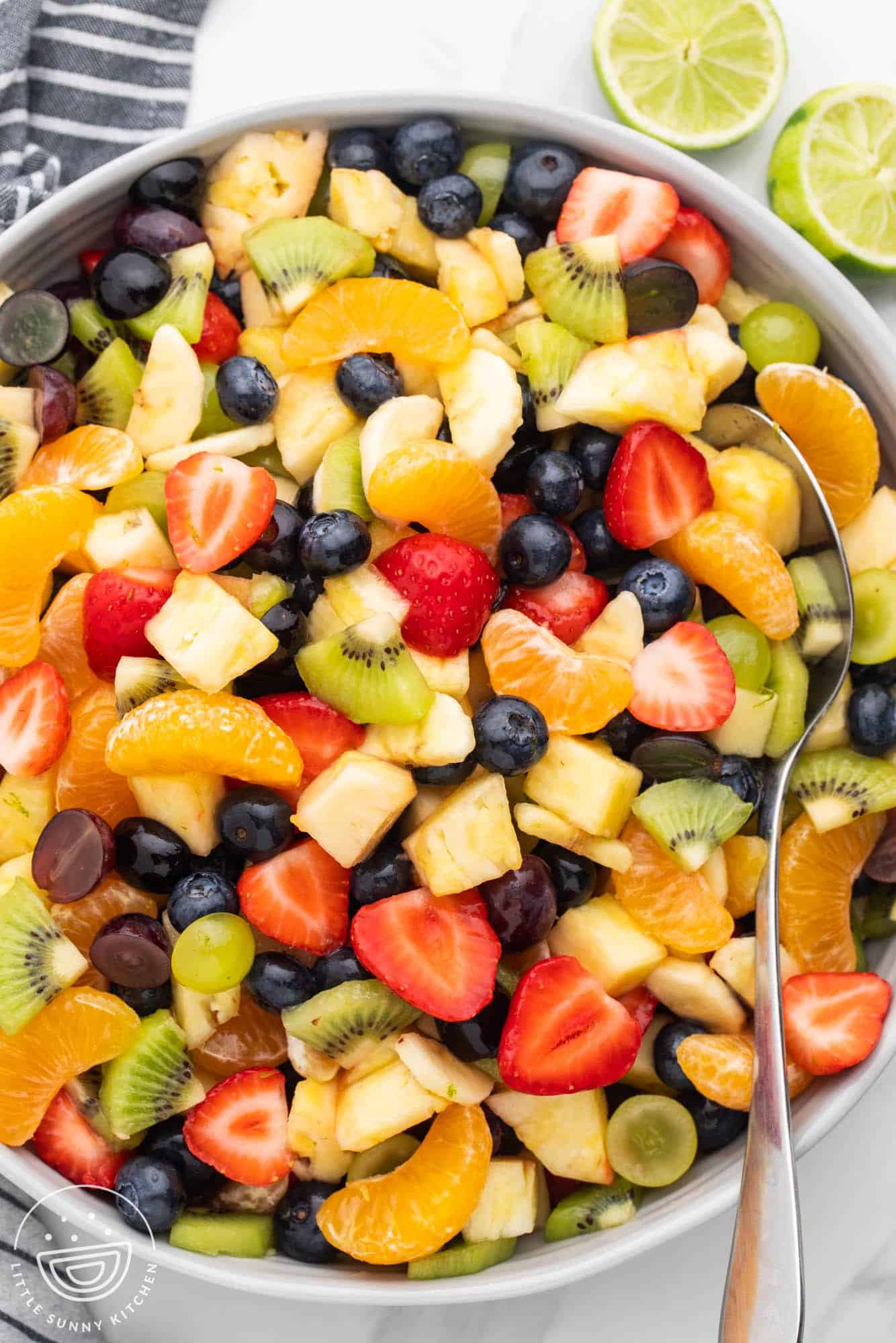 Overhead shot of a fruit salad with lime honey dressing in a large gray bowl, and a serving spoon