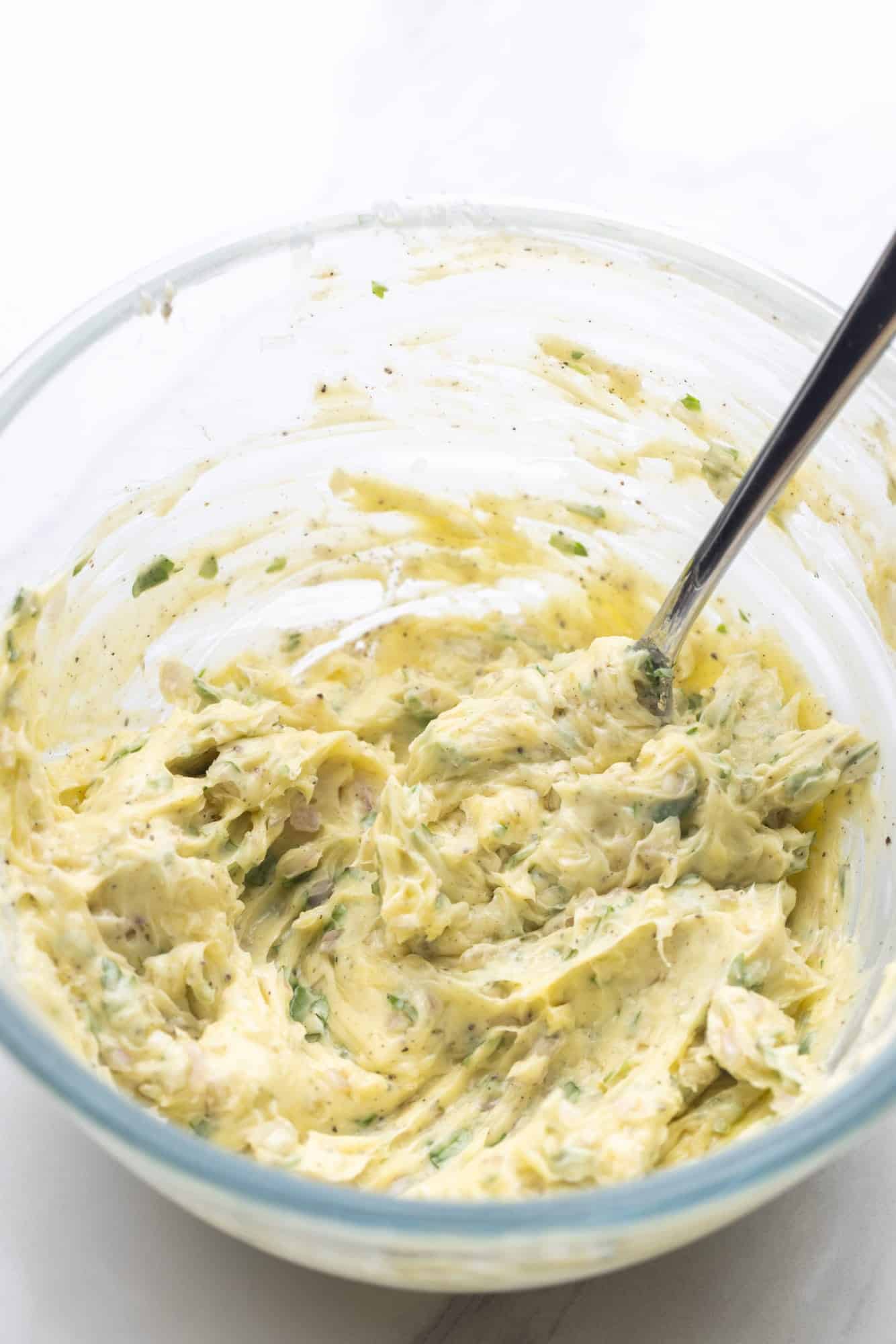 Herb butter mixed together in a bowl with a spoon.