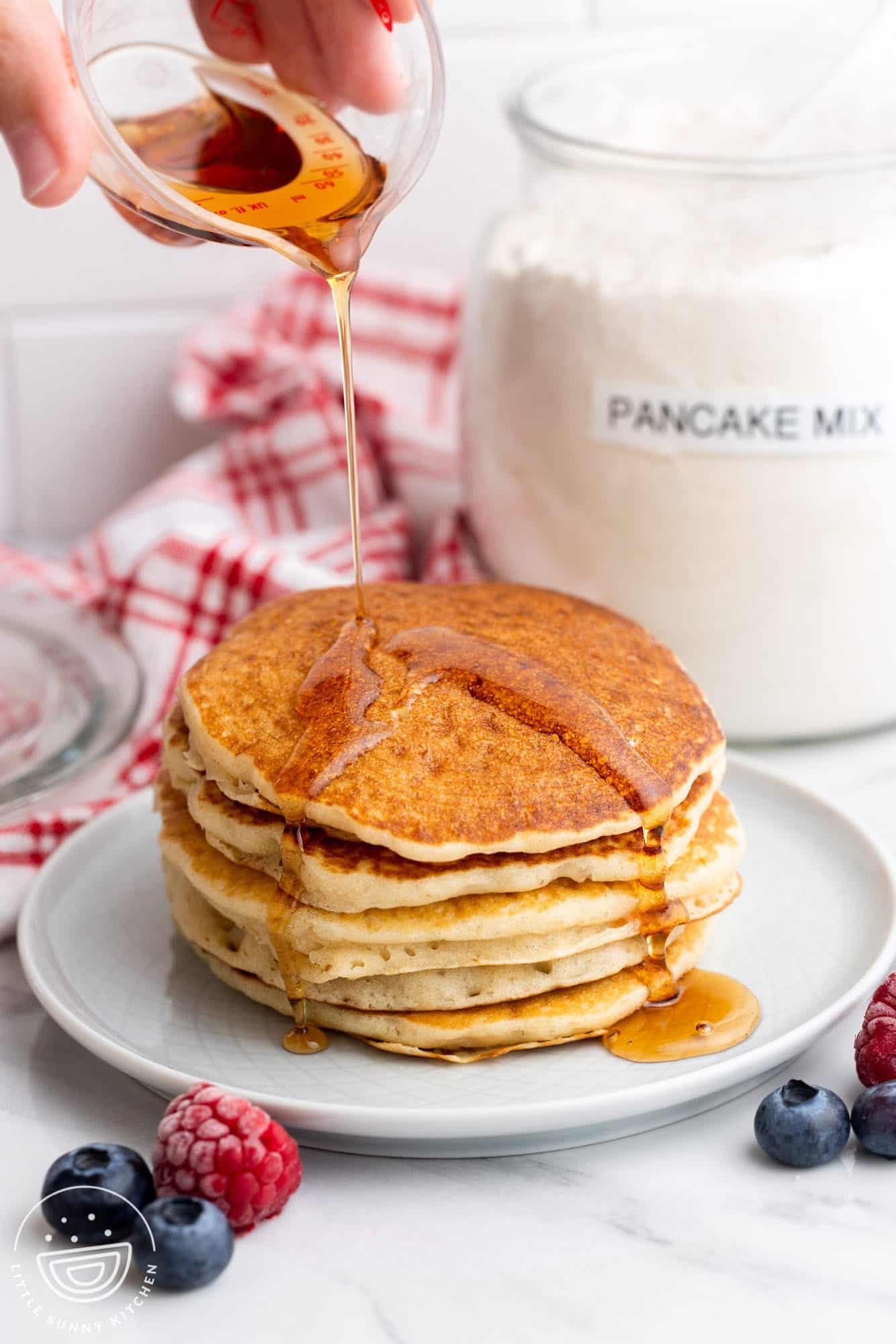 A stack of homemade pancakes on a plate with syrup. In the background is a jar of homemade pancake mix.