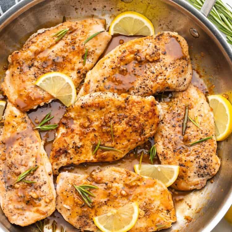 seared chicken cutlets in a skillet with a savory pan sauce, rosemary sprigs, and sliced lemon wedges.