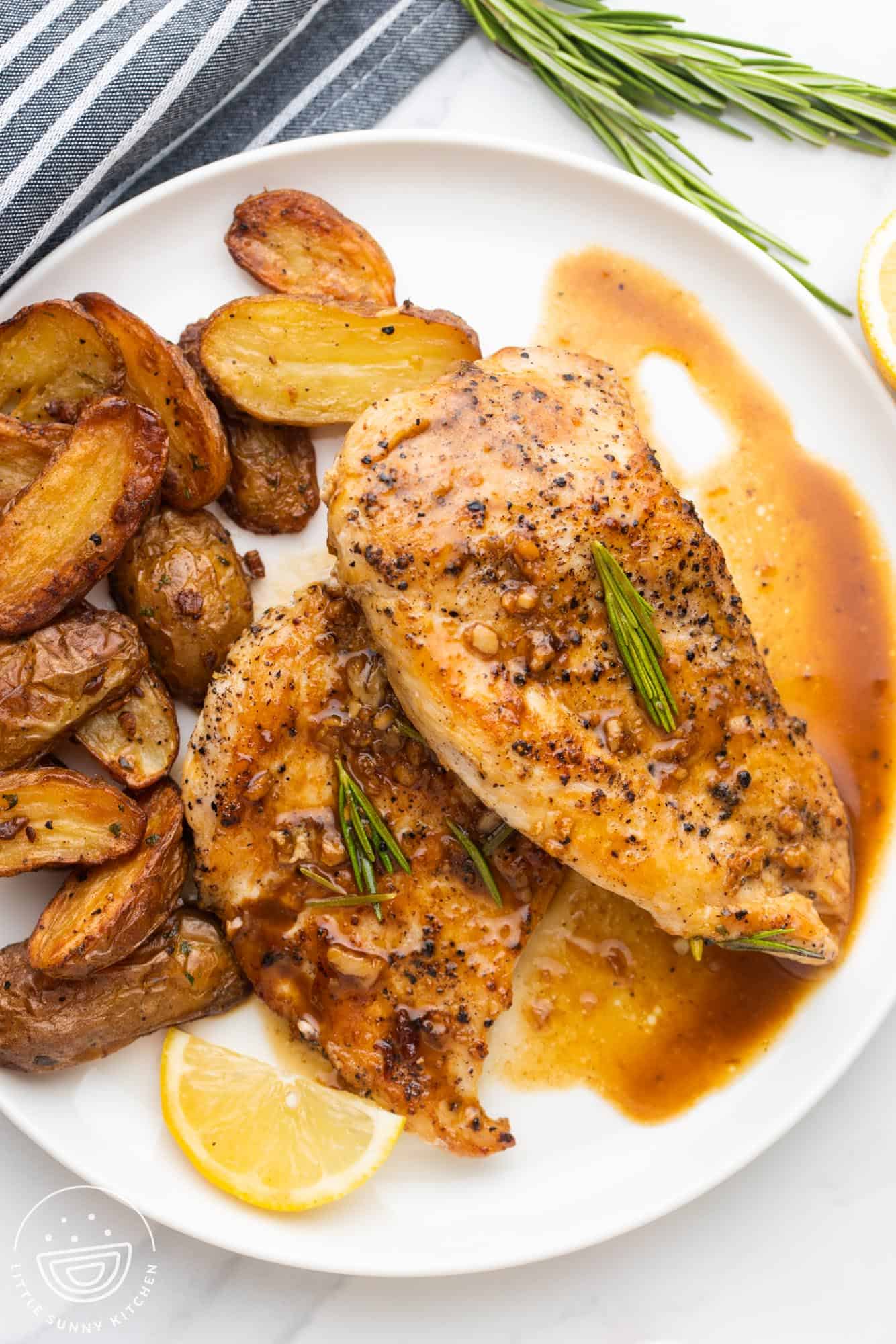 two pieces of lemon rosemary chicken on a plate with sauce and roasted fingerling potatoes.