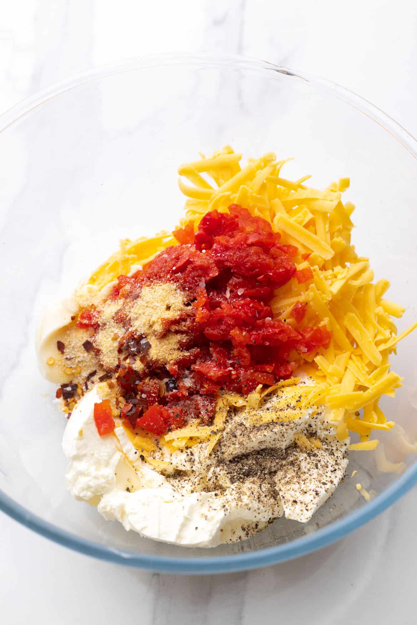 The ingredients to make pimento cheese in a glass mixing bowl