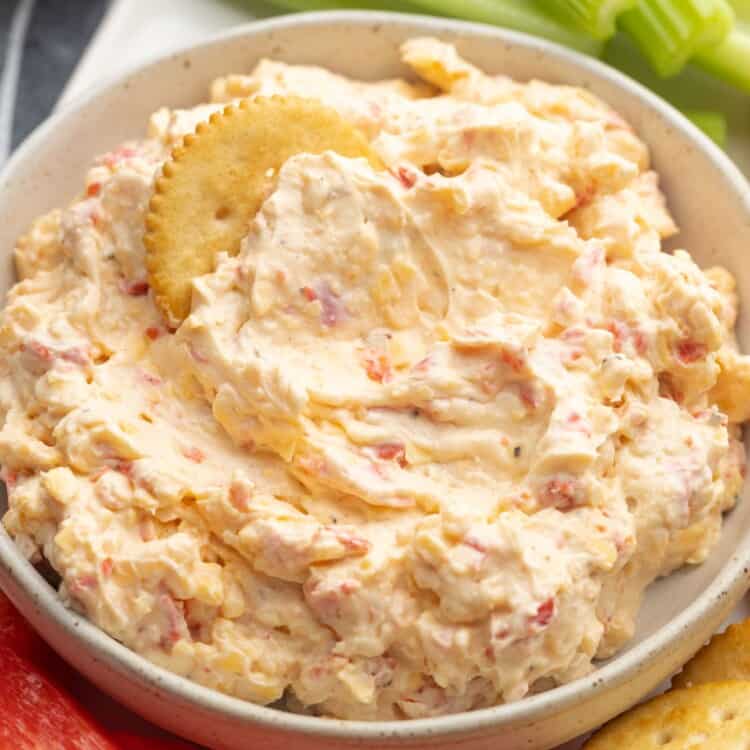 a bowl of pimento cheese next to celery sticks, red peppers, and crackers.