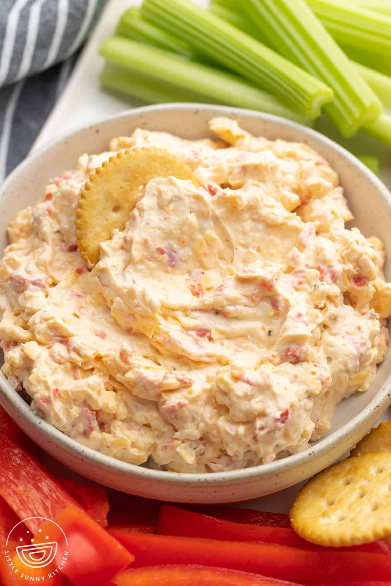 a bowl of pimento cheese next to celery sticks, red peppers, and crackers. 