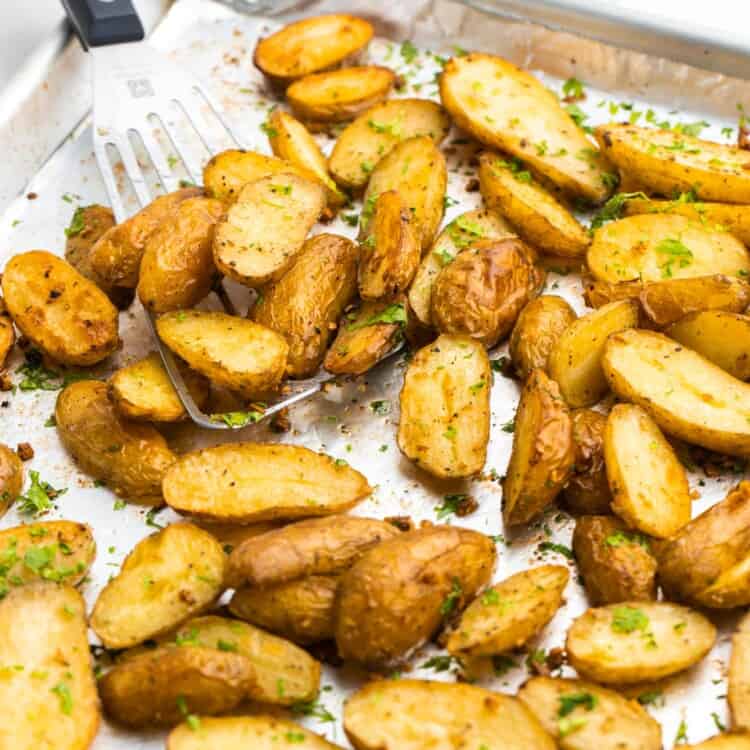 Roasted fingerling potatoes on a sheet pan, with a serving spatula on the side