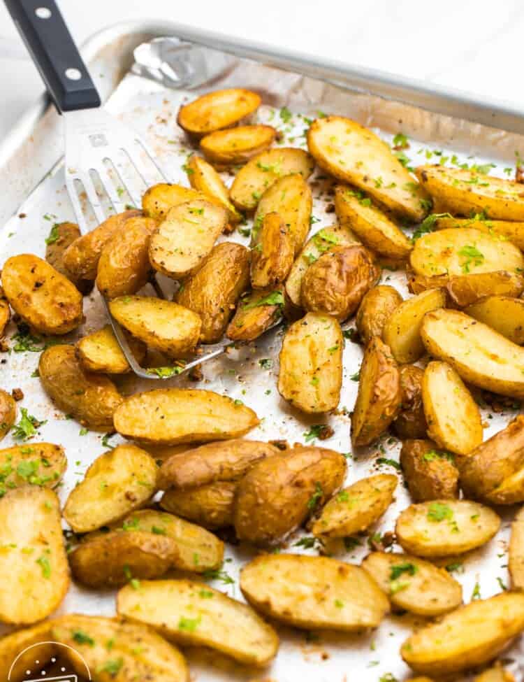 Roasted fingerling potatoes on a sheet pan, with a serving spatula on the side