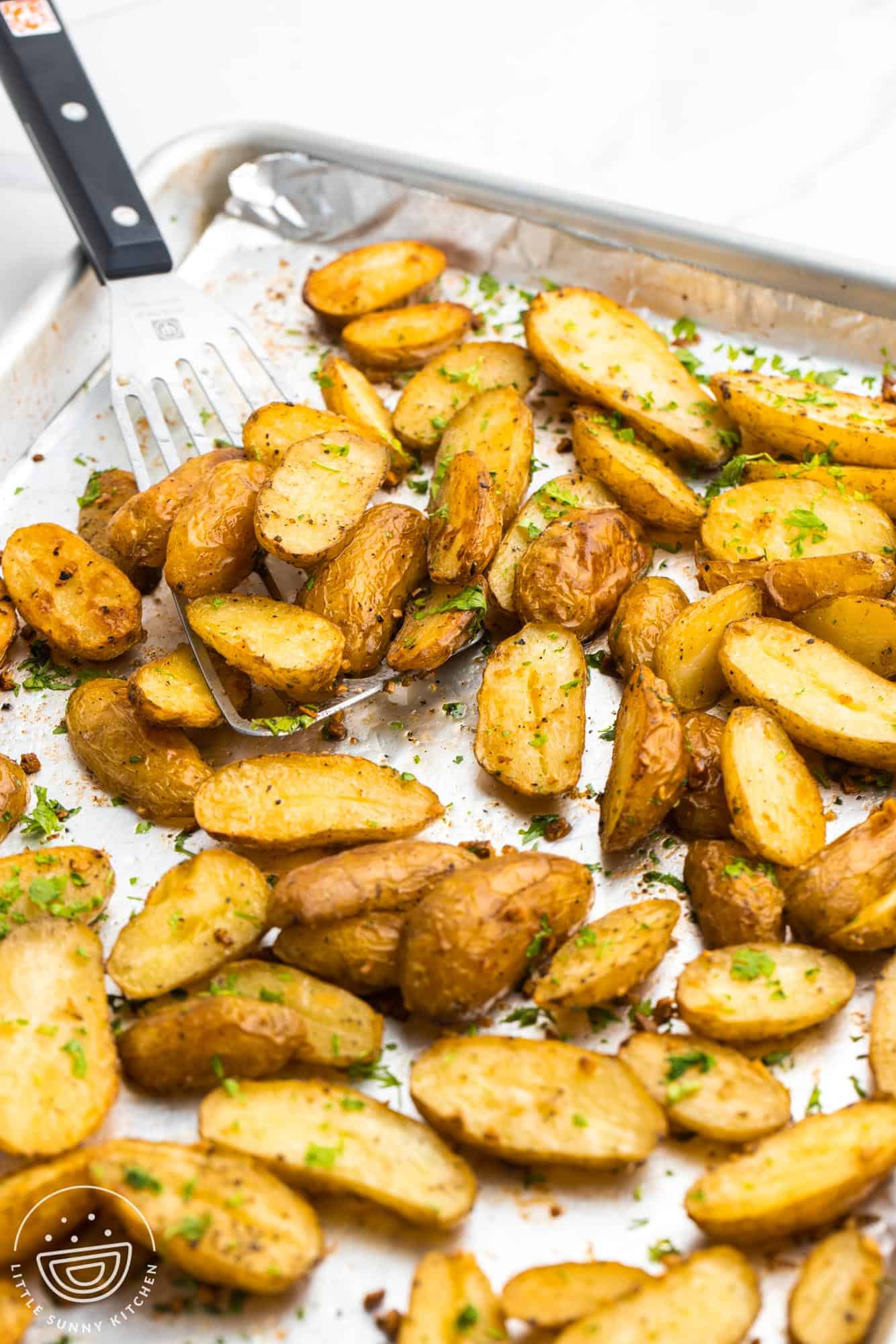 Roasted fingerling potatoes on a sheet pan, with a serving spatula on the side