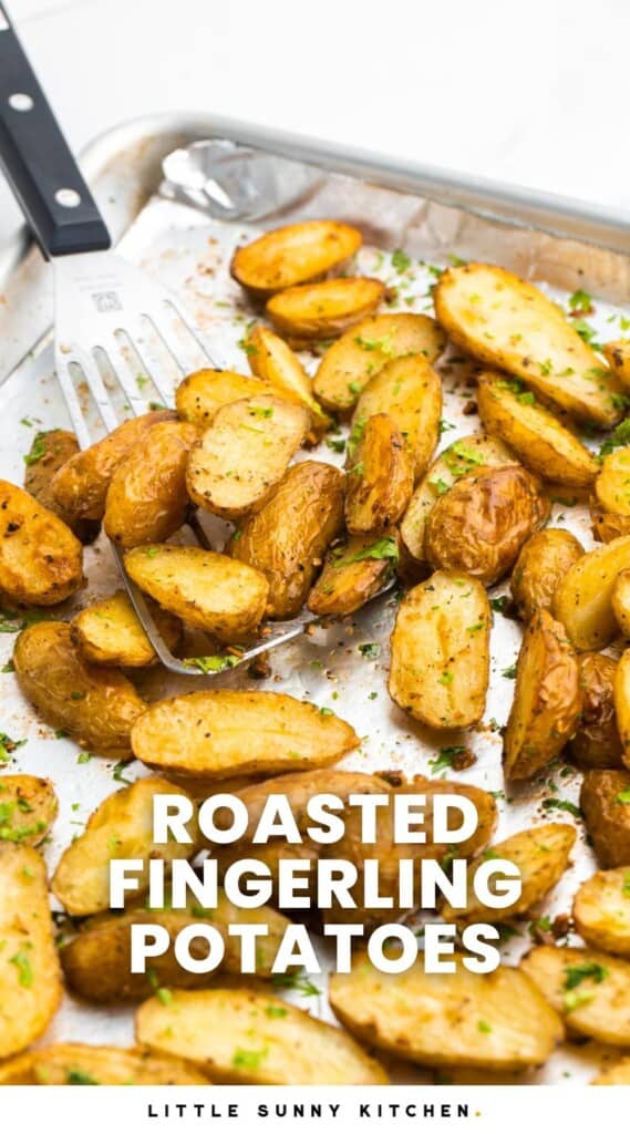 Roasted fingerling potatoes on a sheet pan, with a serving spatula on the side. And overlay text that says "Roasted Fingerling Potatoes"