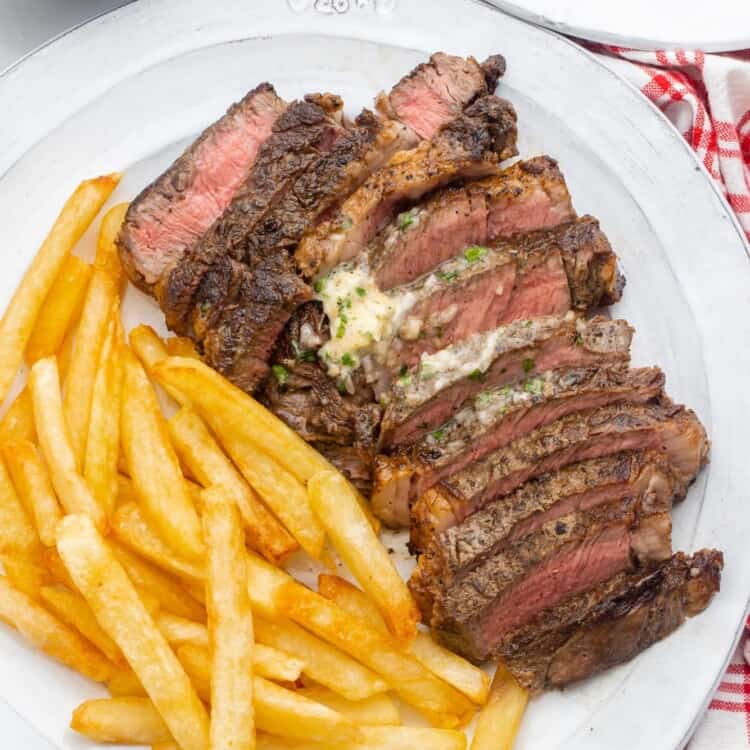 A plate of sliced steak with herb butter and crispy french fries.