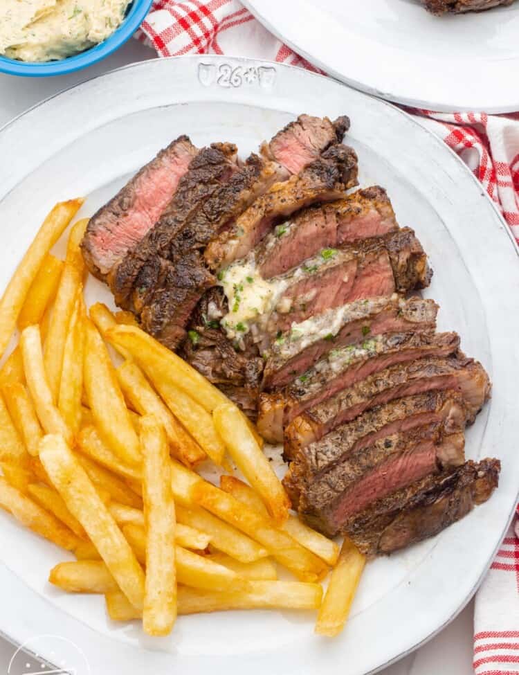 A plate of sliced steak with herb butter and crispy french fries.