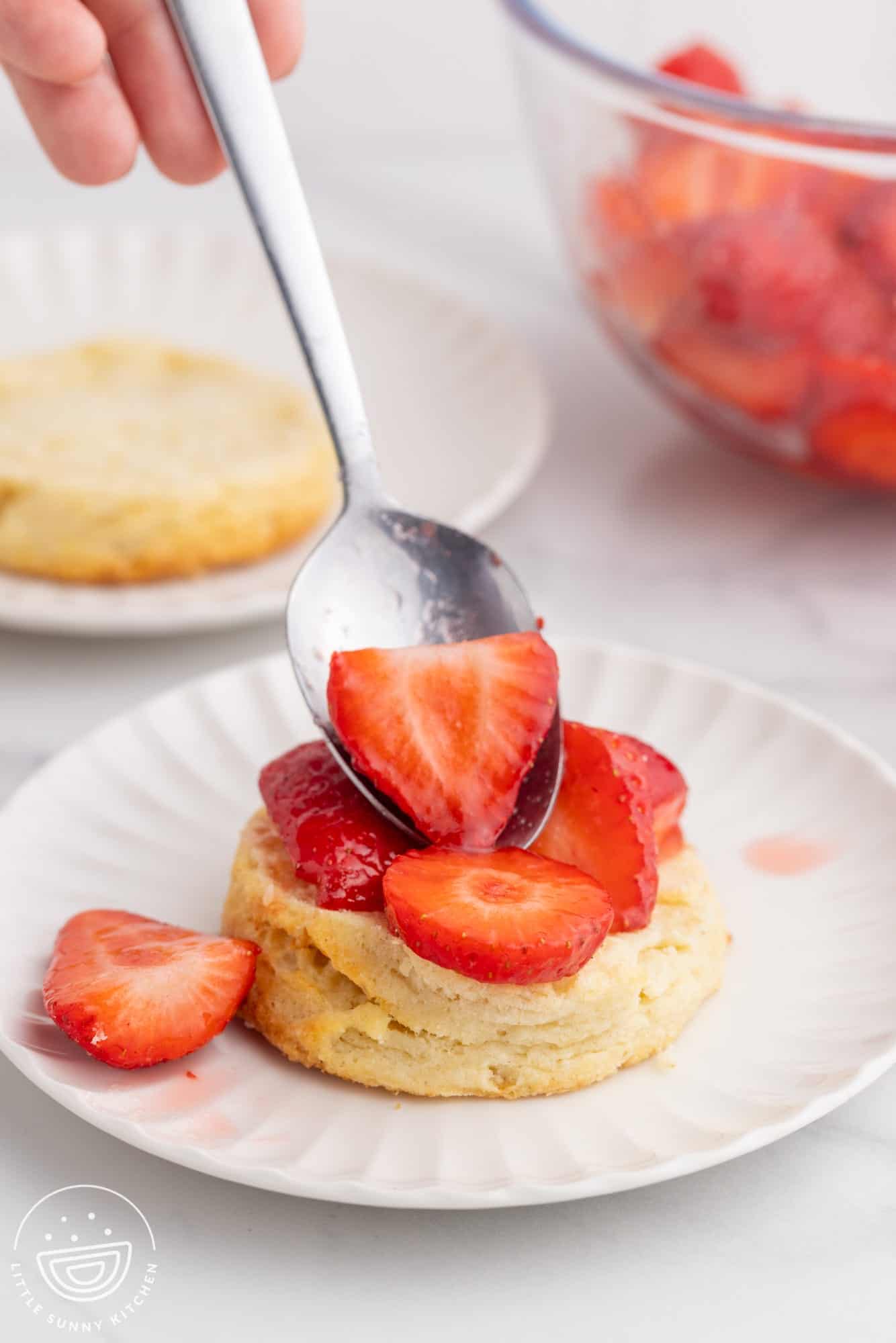 Spooning macerated strawberries over homemade biscuits